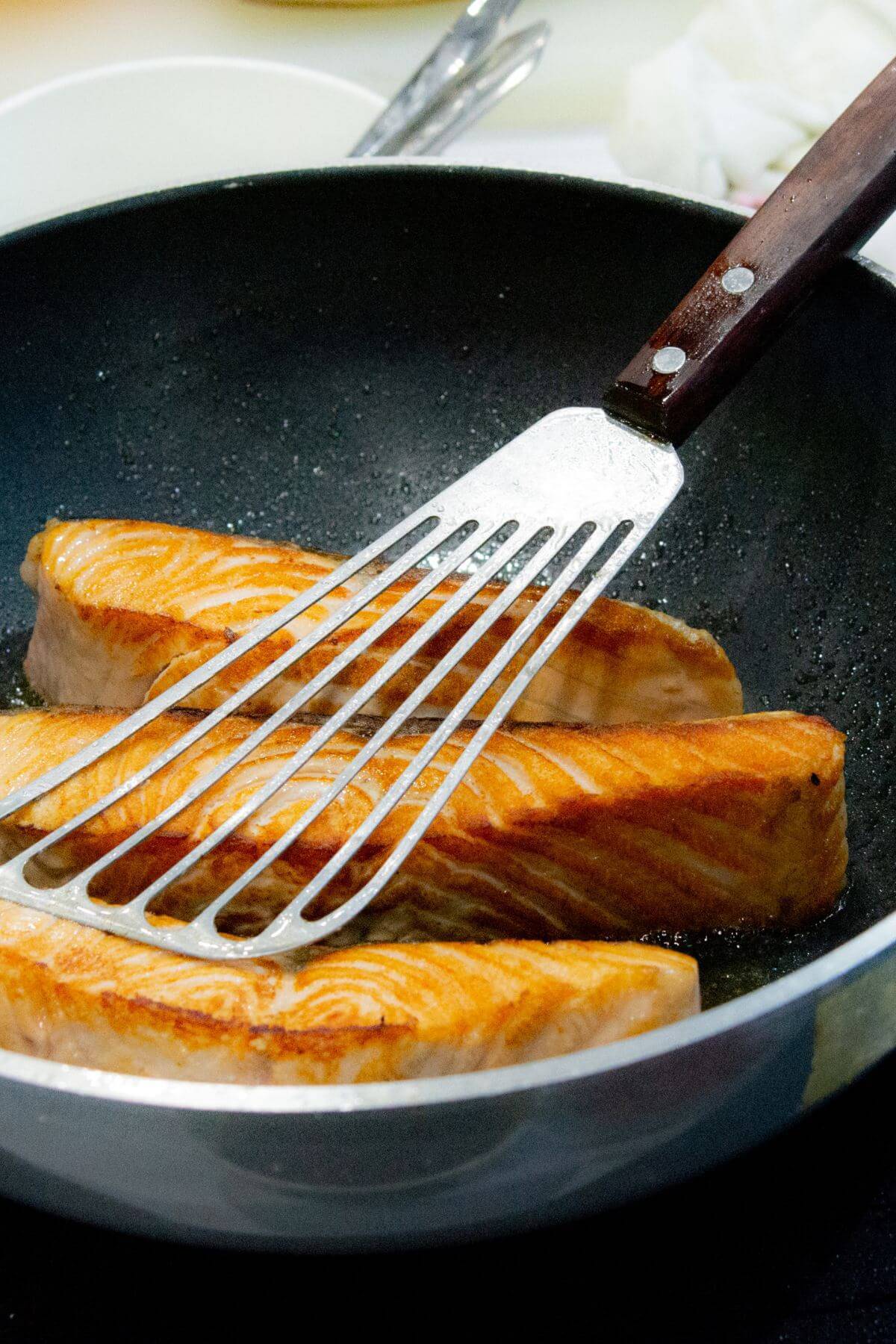 3 pieces of salmon cooking in a pan