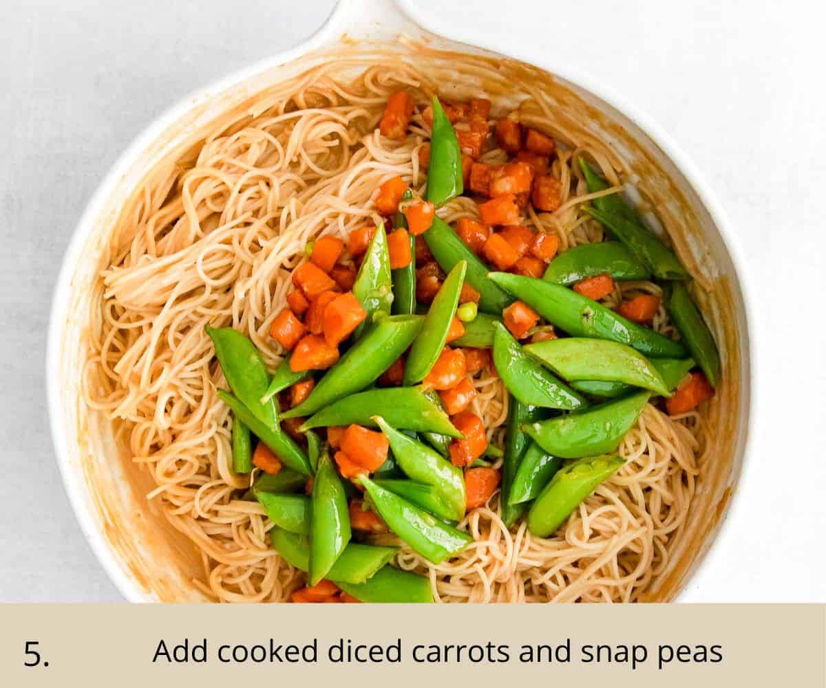 diced carrots and snap peas in a bowl with noodles and peanut sauce