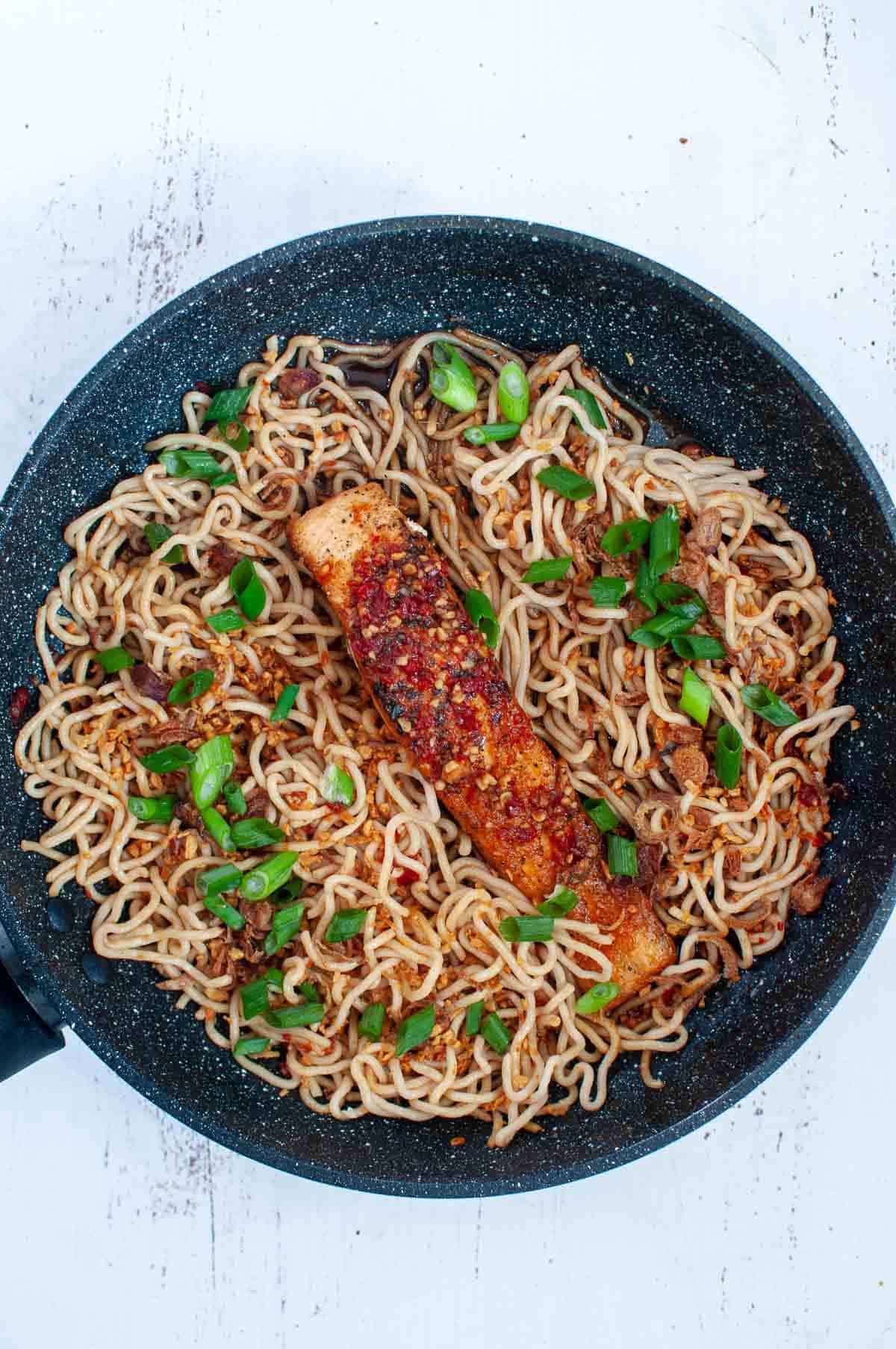 salmon with noodles and spring onions in a pan