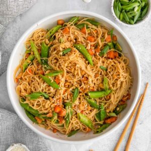 a white bowl with spicy peanut butter noodles scatter with sesame seeds