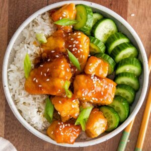 garlic soy chicken bites in a bowl with rice and cucumber