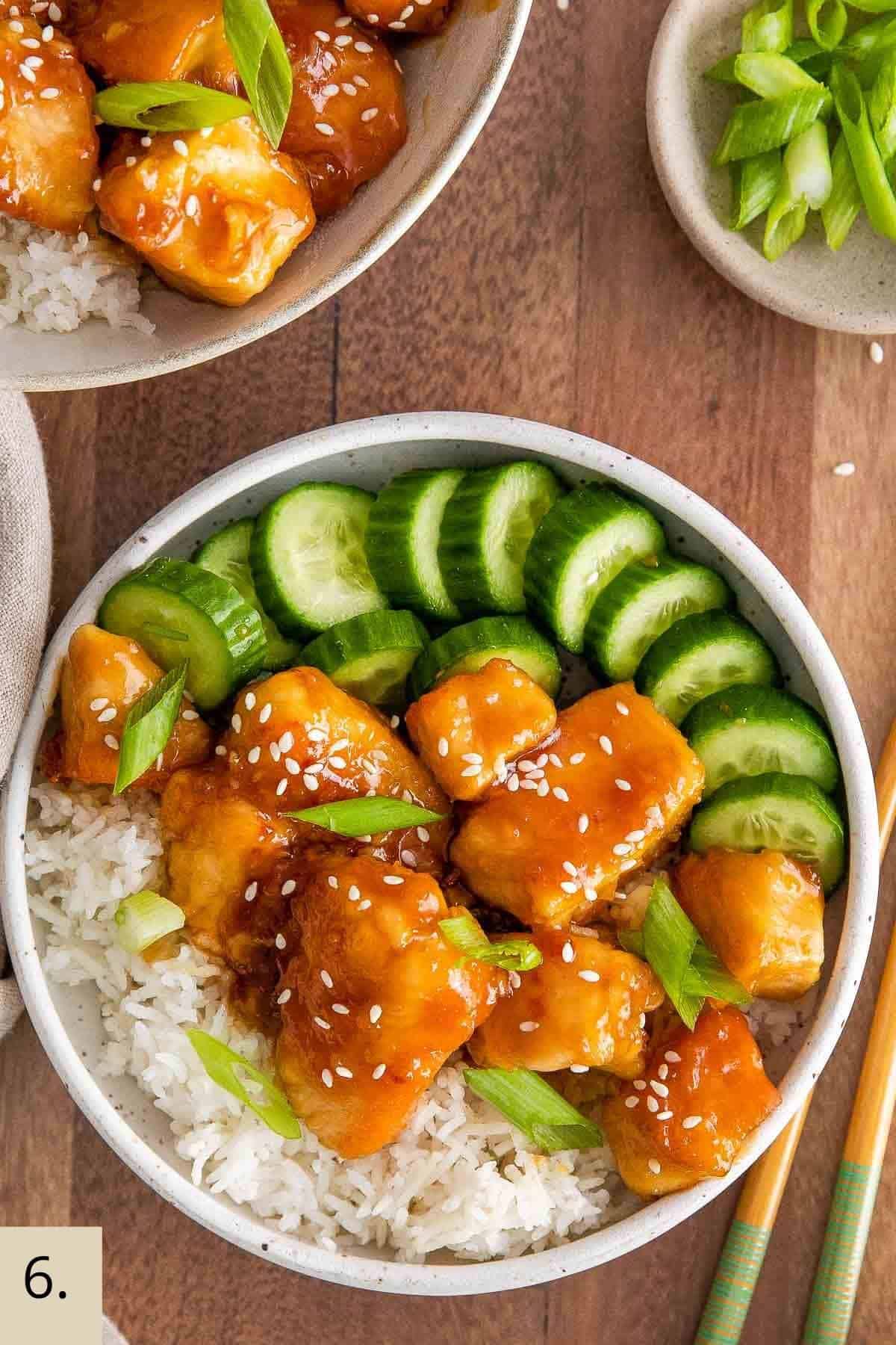 a bowl of sticky glazed honey garlic chicken with green onions and cucumber