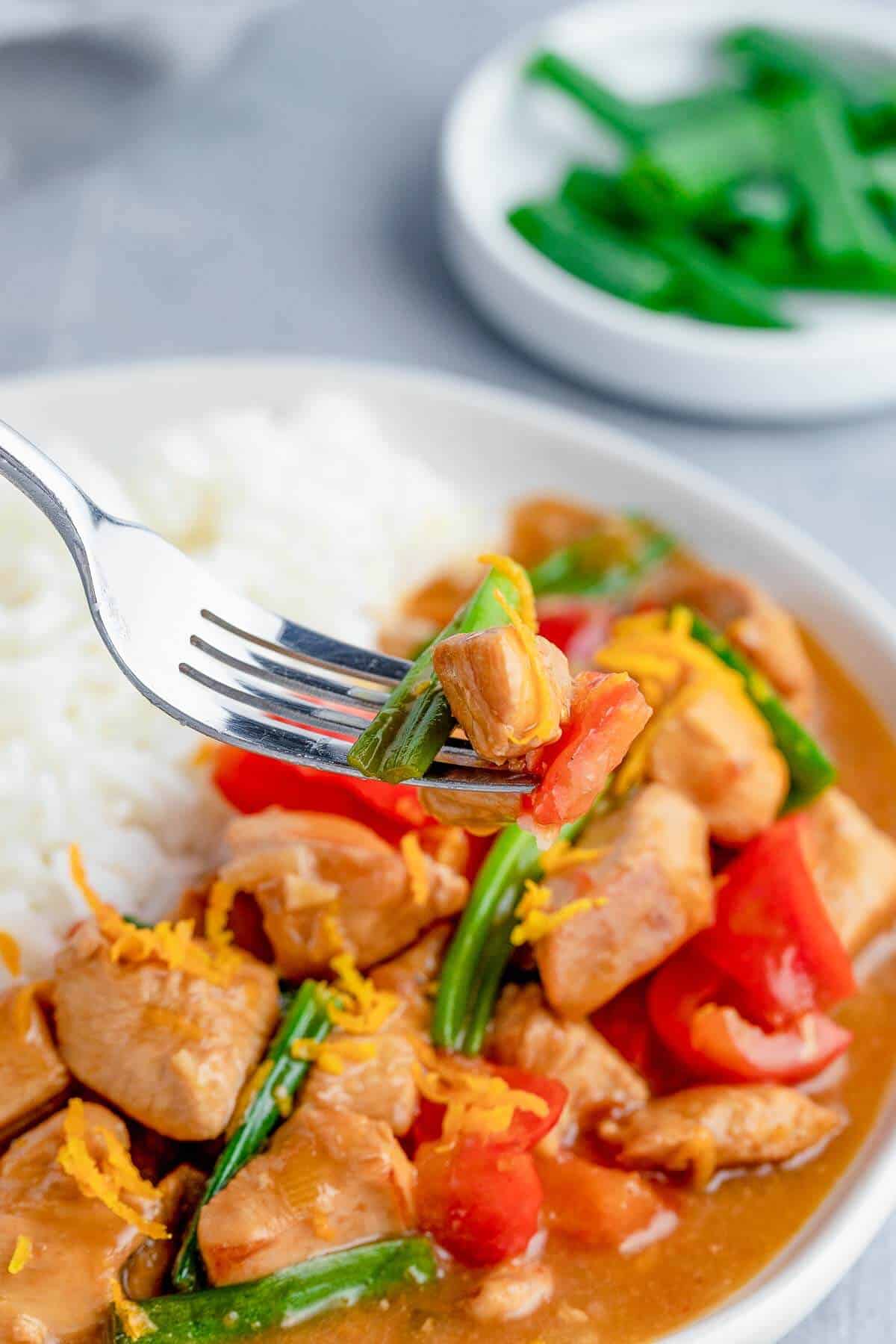 orange chicken on a fork with plate in background