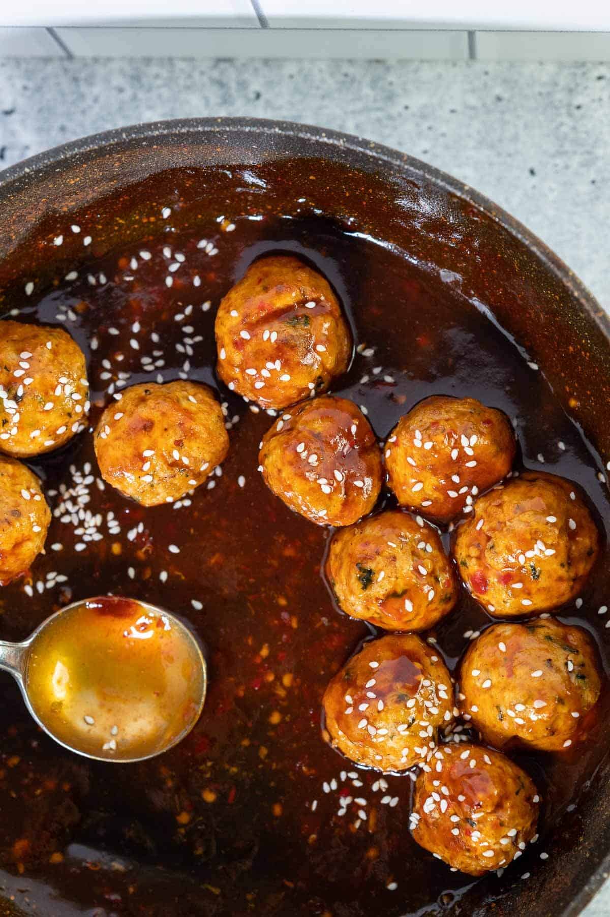 asian chicken meatballs in a skillet with spoon and sauce