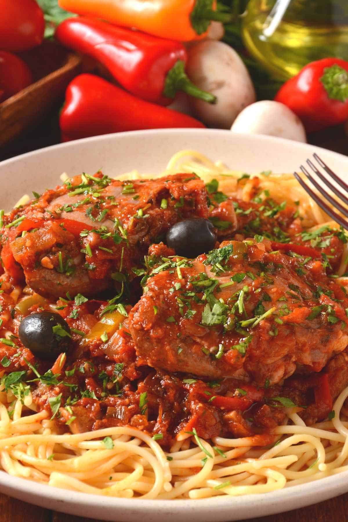 a white plate with chicken caccitore and spaghetti