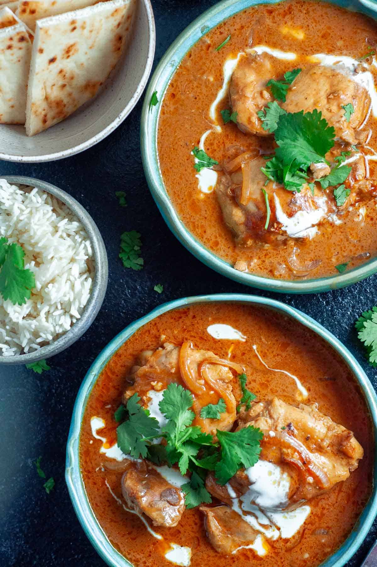 two bowls of healthy butter chicken with rice, naan and corriander