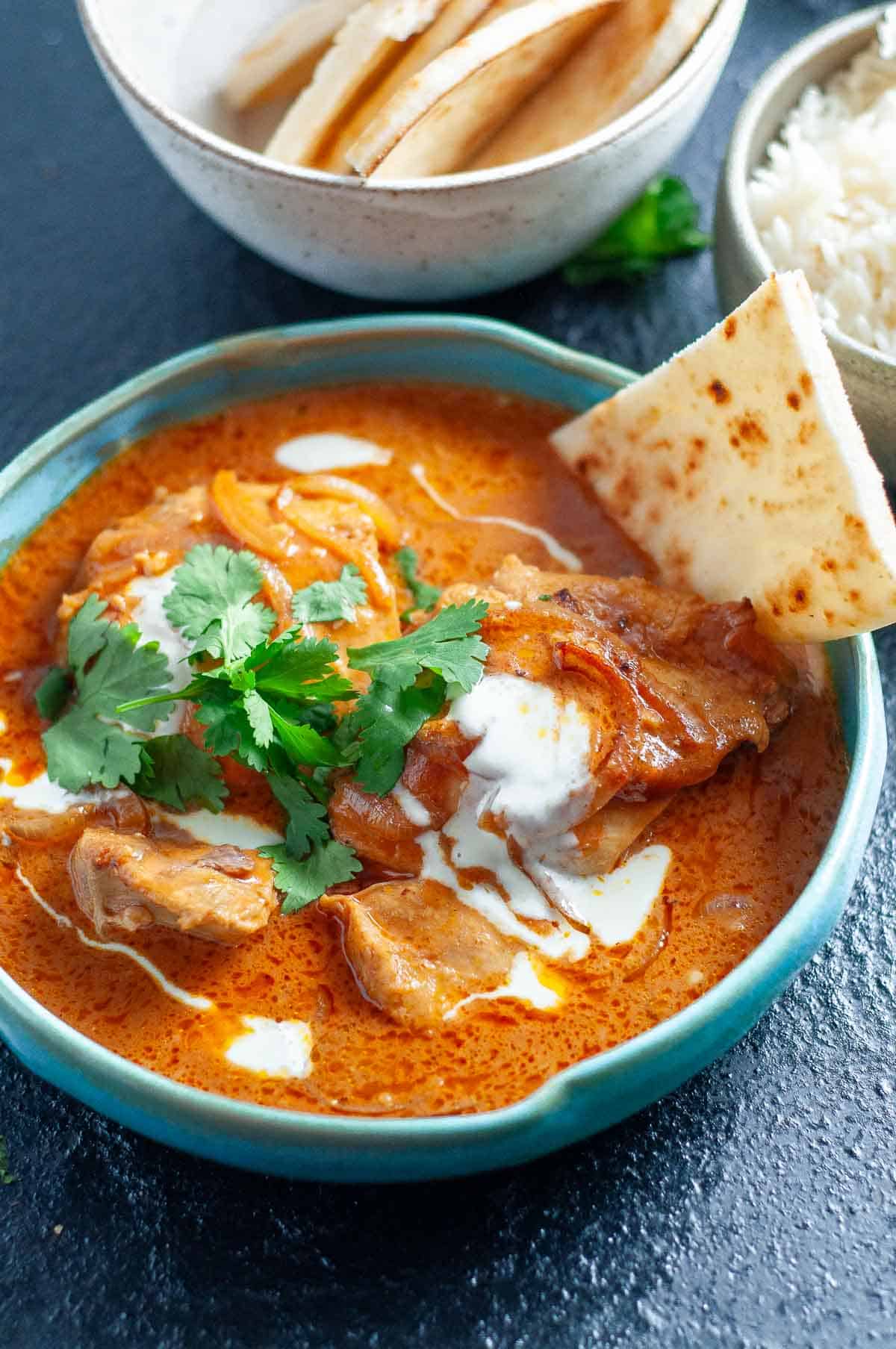 blue bowl with butter chicken, naan and corriander