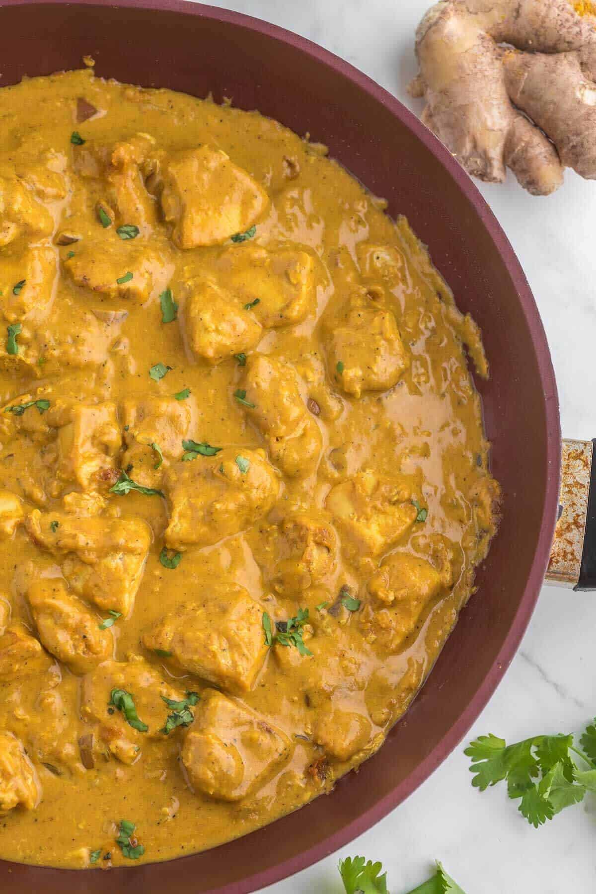 creamy chicken curry in a skillet with parsley garnish