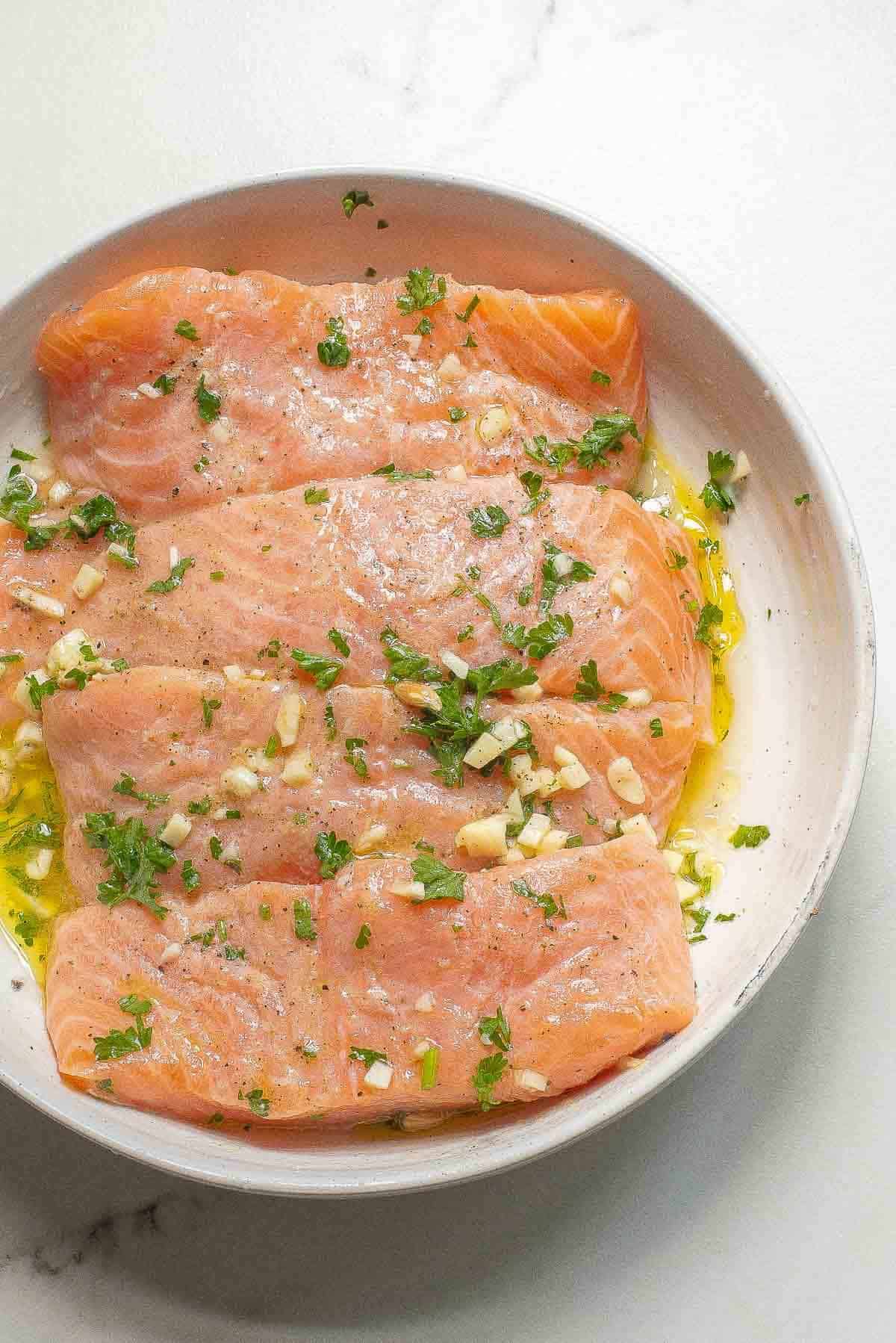 four skinless salmon filets marinating in oil and garlic and lemon