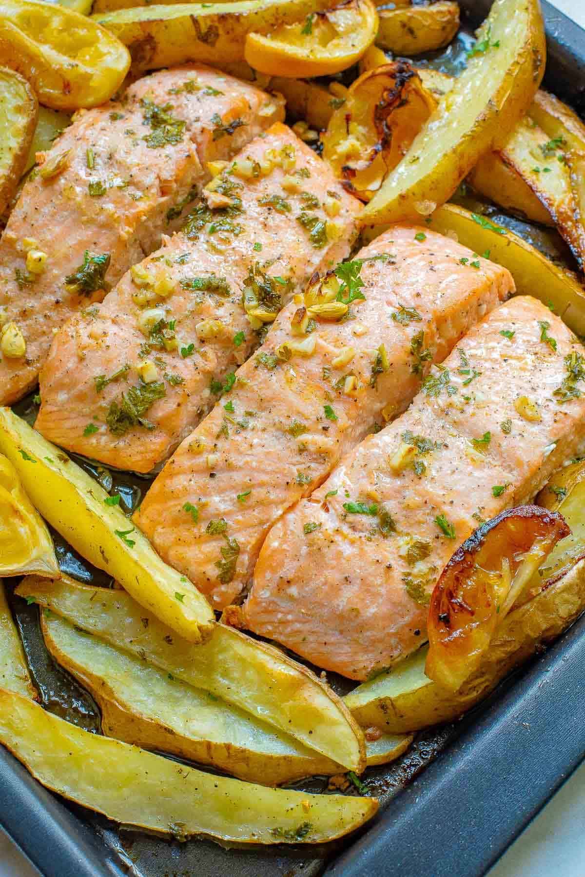 cooked salmon filets and potato wedges on a sheet pan