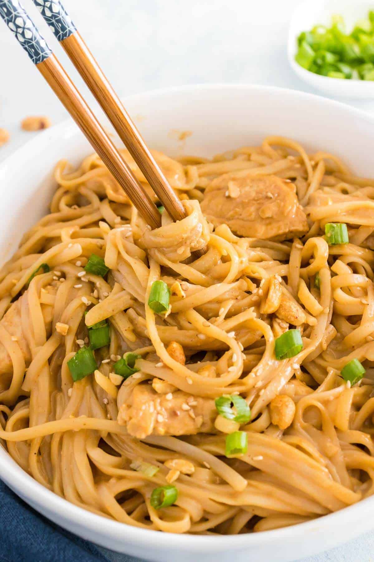 chopsticks dipped into a bowl of peanut butter rice noodles