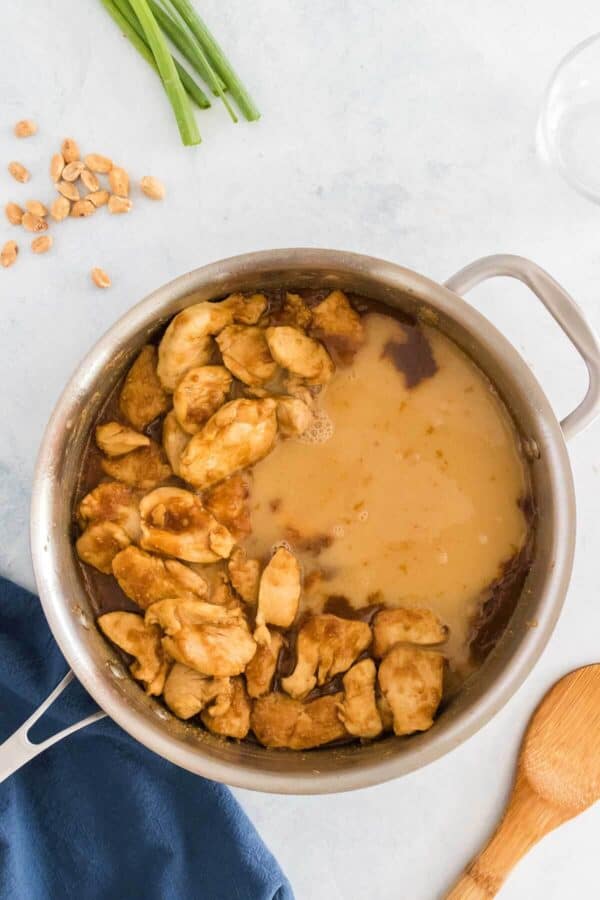 a skillet with chicken in peanut butter sauce