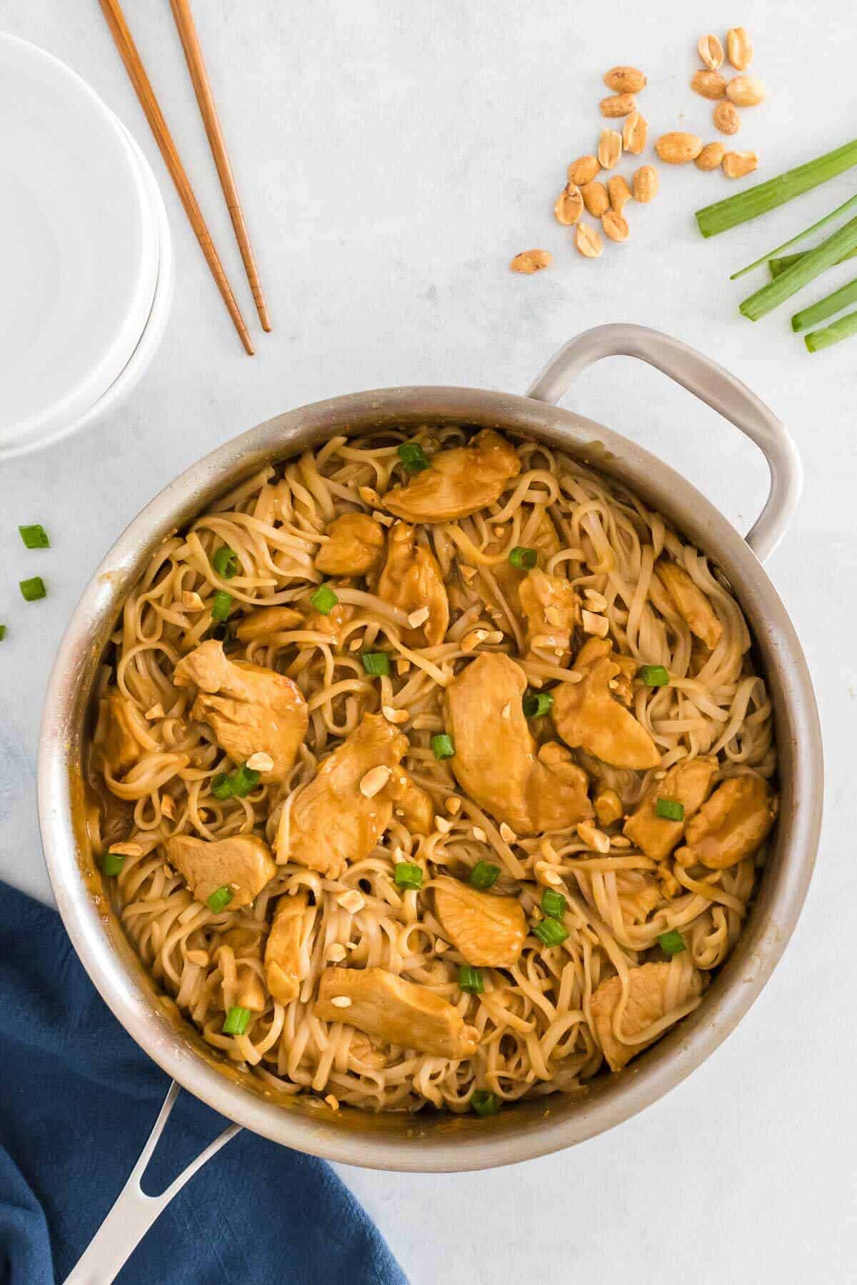 a skillet with noodles, peanut sauce and chicken