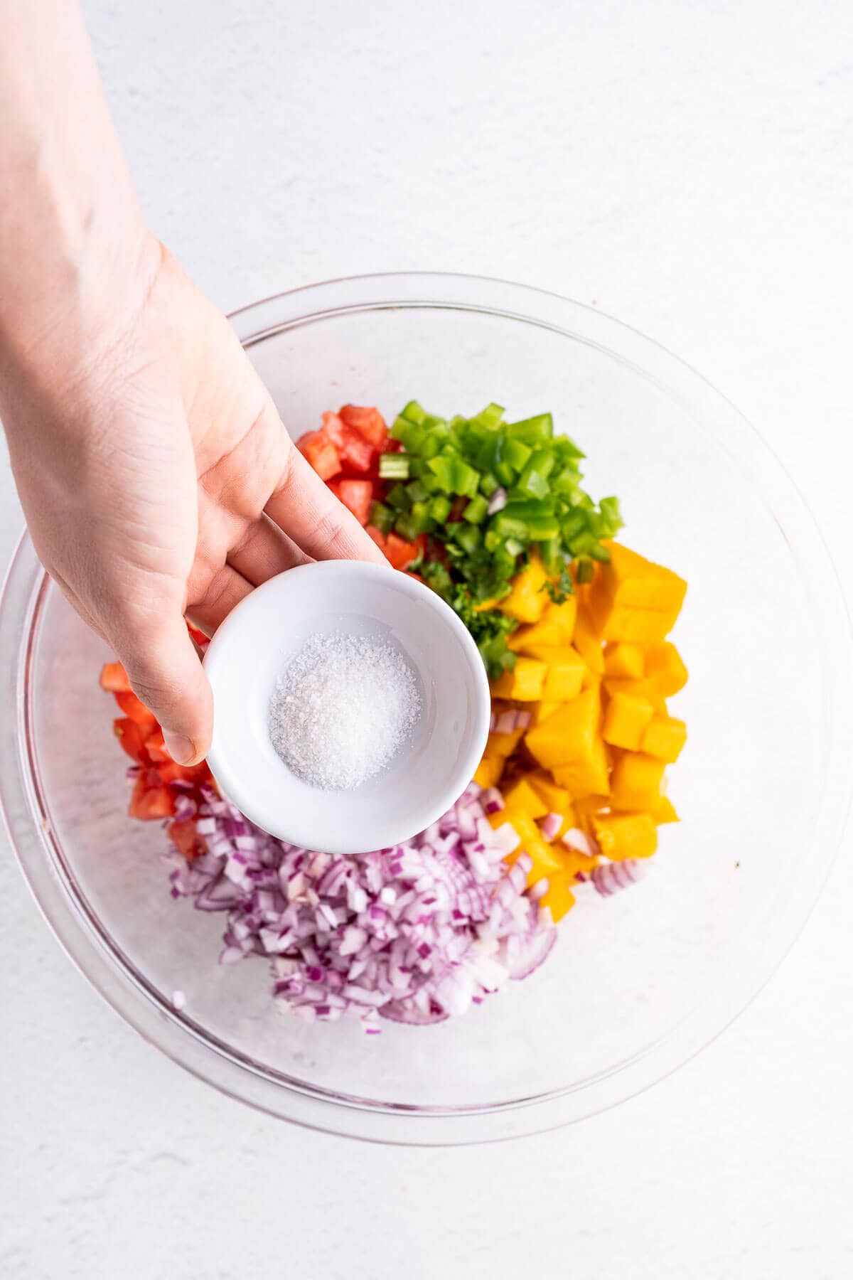 adding sea salt to spicy salsa with mango, onions and tomatoes