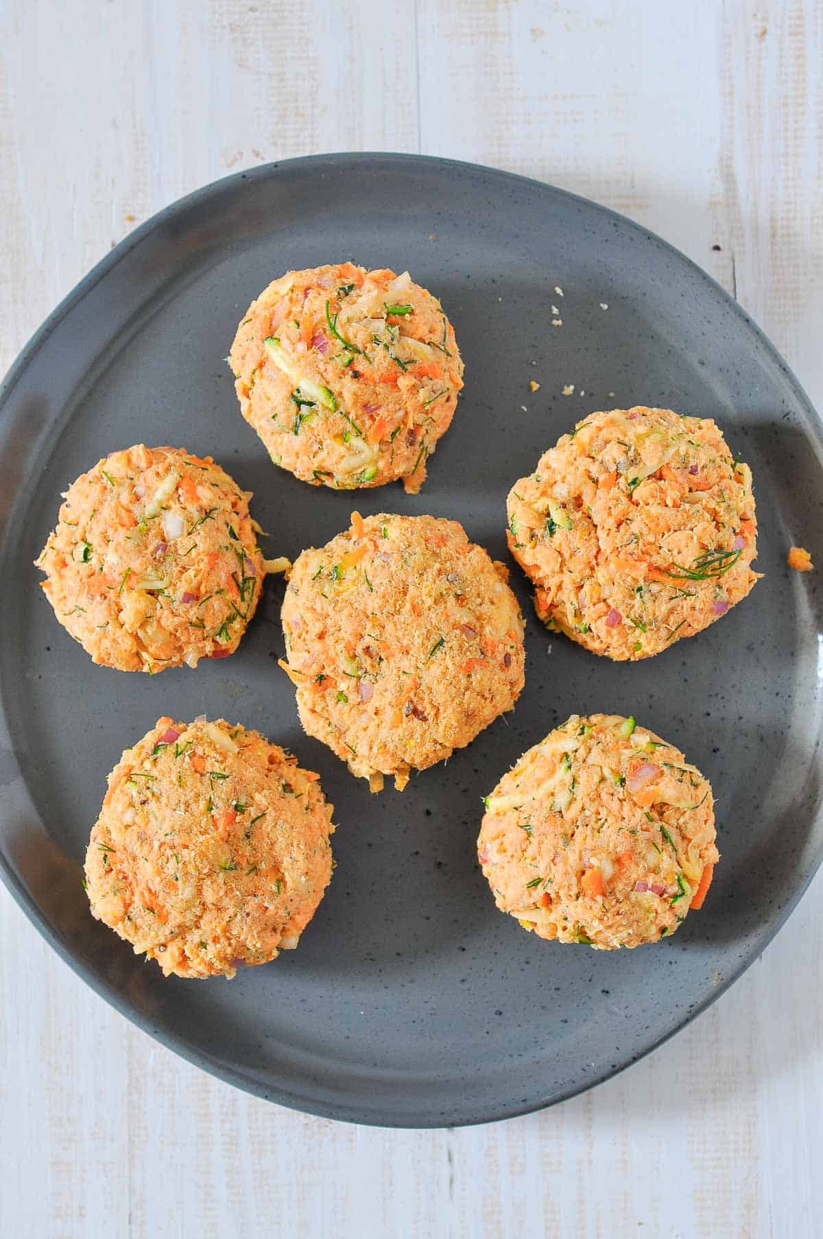 6 salmon fritters uncooked on a grey plate