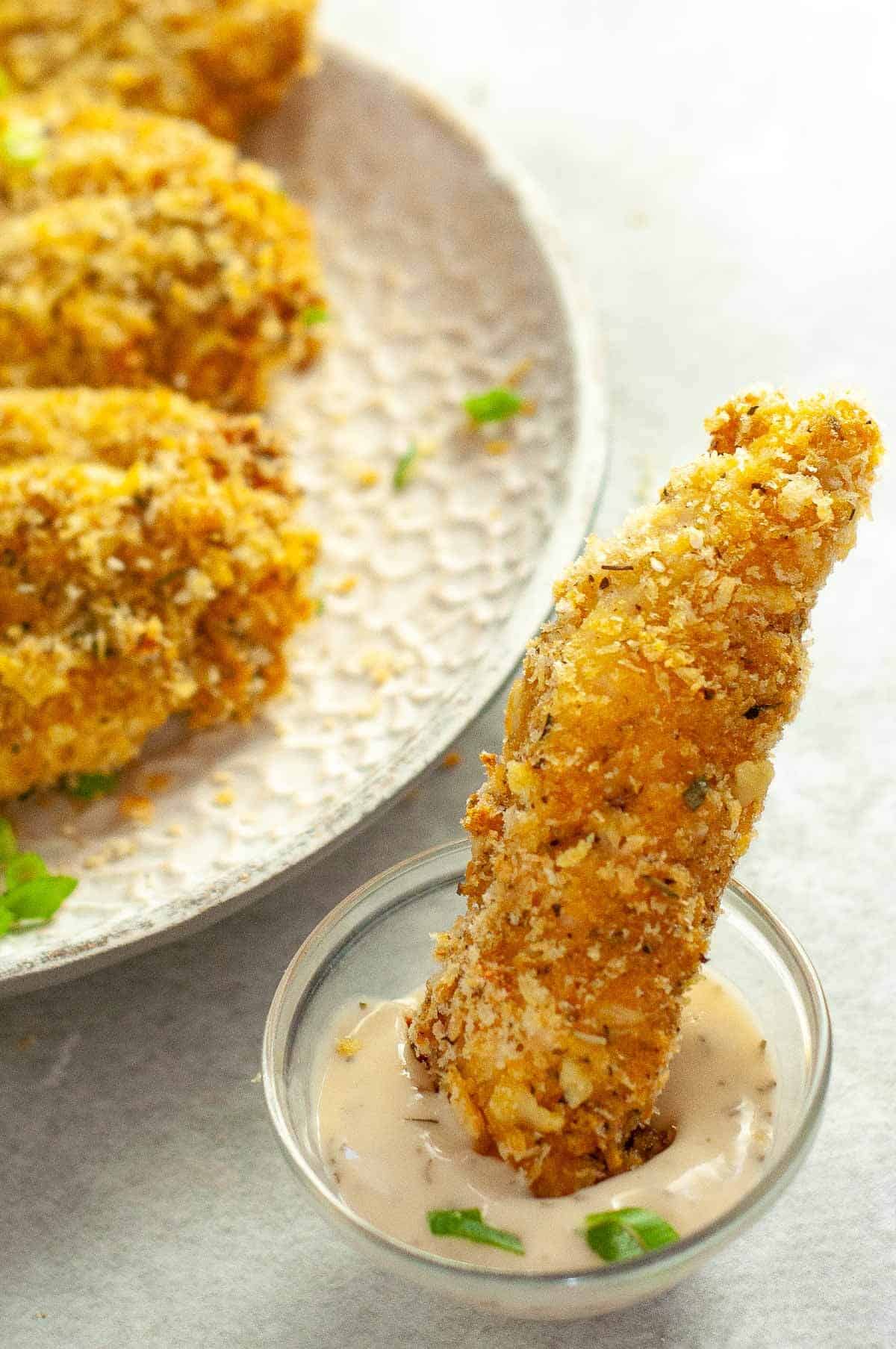 one chicken finger in a bowl of dipping sauce