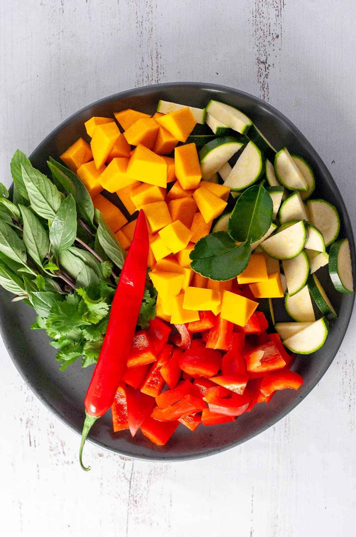 A plate with diced pumpkin, capsicum, chili, zucchini and thai basil