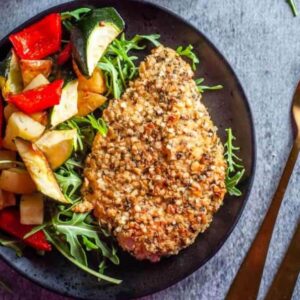 quinoa crusted chicken on a black plate with vegetables