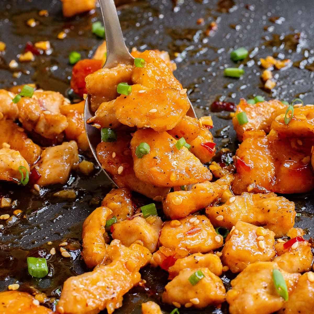 spoon scooping up sweet and spicy chicken bites from sheet pan