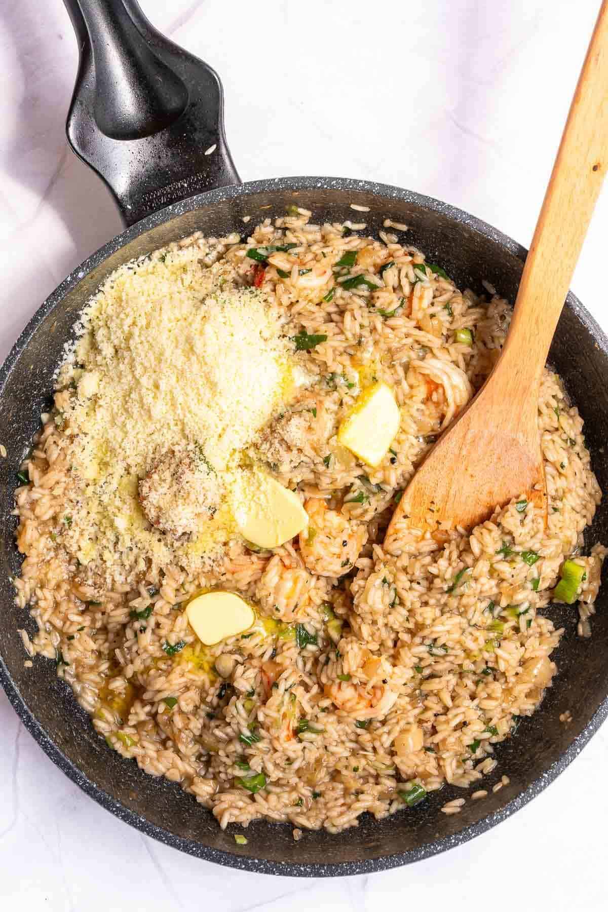 adding parmesan and butter to a skillet of risotto
