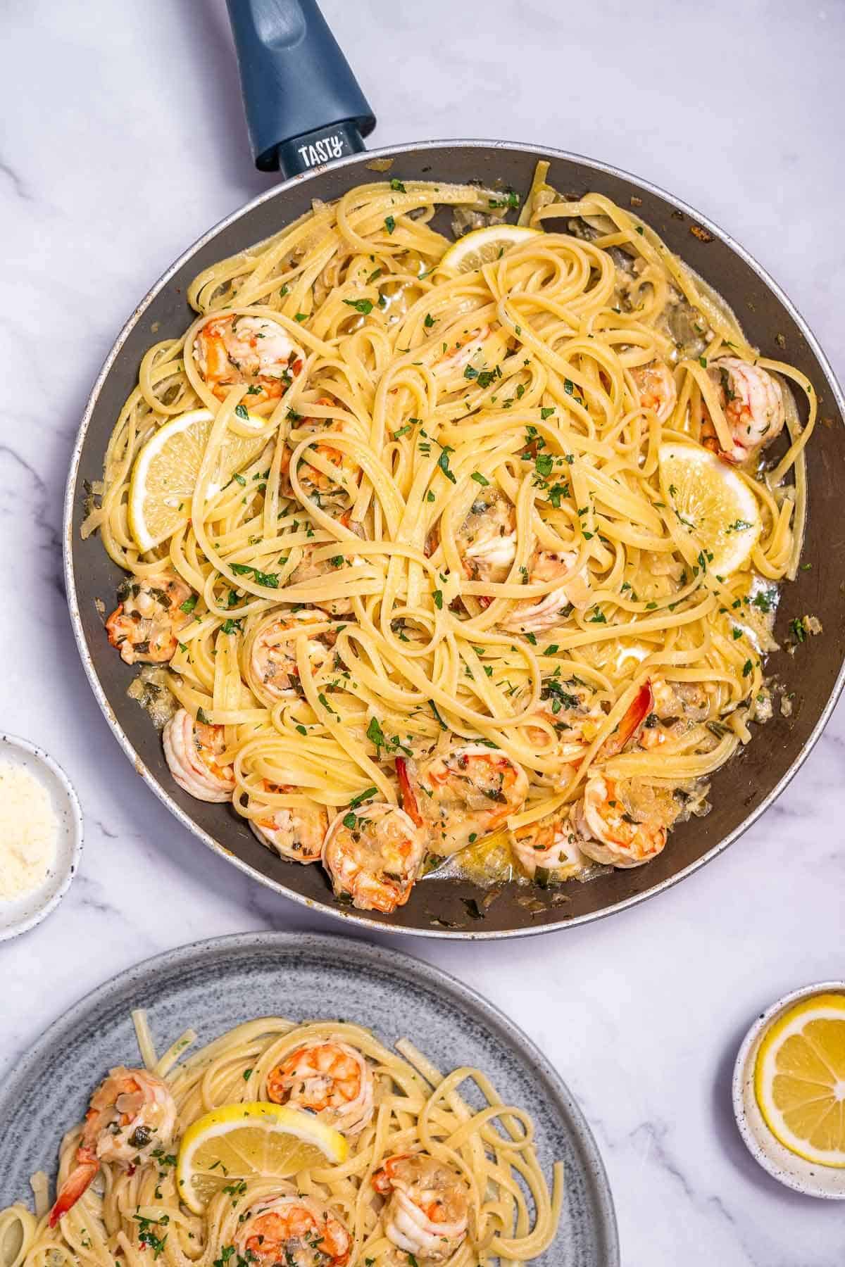 a skillet and plate with prawn pasta overhead on a bench