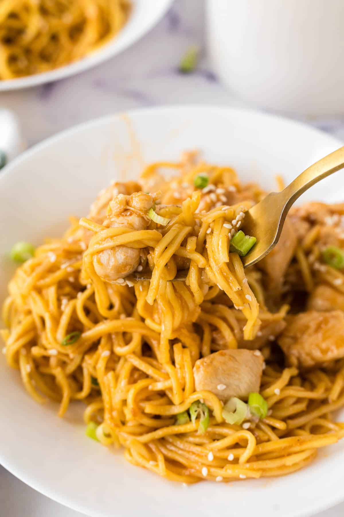 fork scooping up chicken and garlic noodles in a bowl
