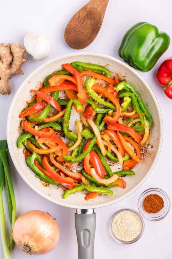 slices of red and green bell peppers cooking in a skillet