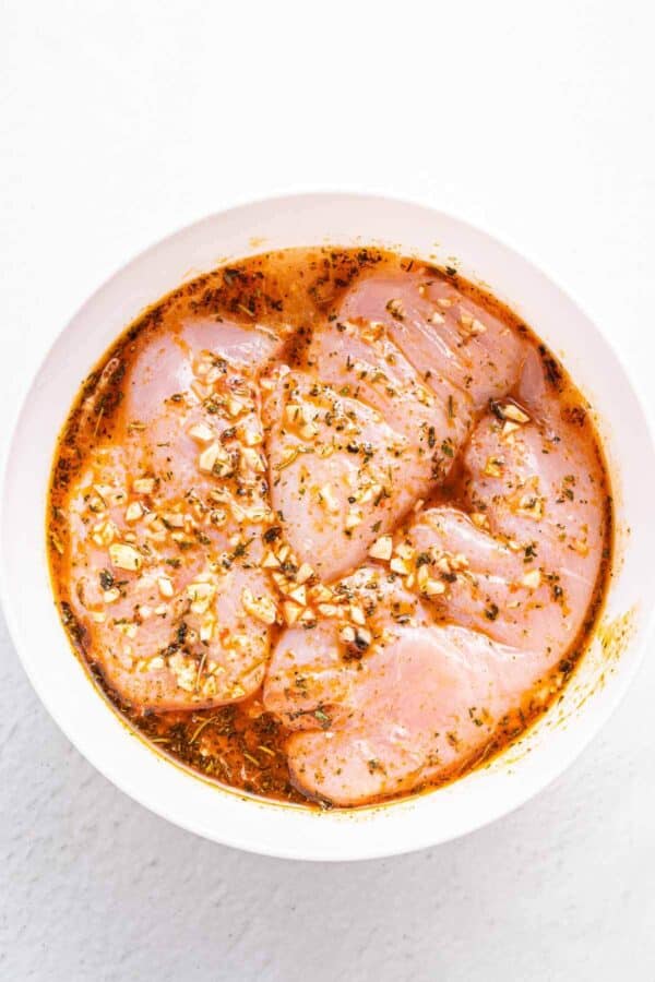 3 raw chicken breasts in a bowl of marinade