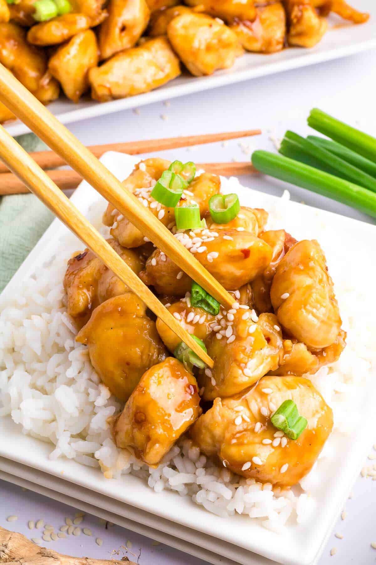 A plate of general tso chicken breast bites with jasmine rice and chopsticks