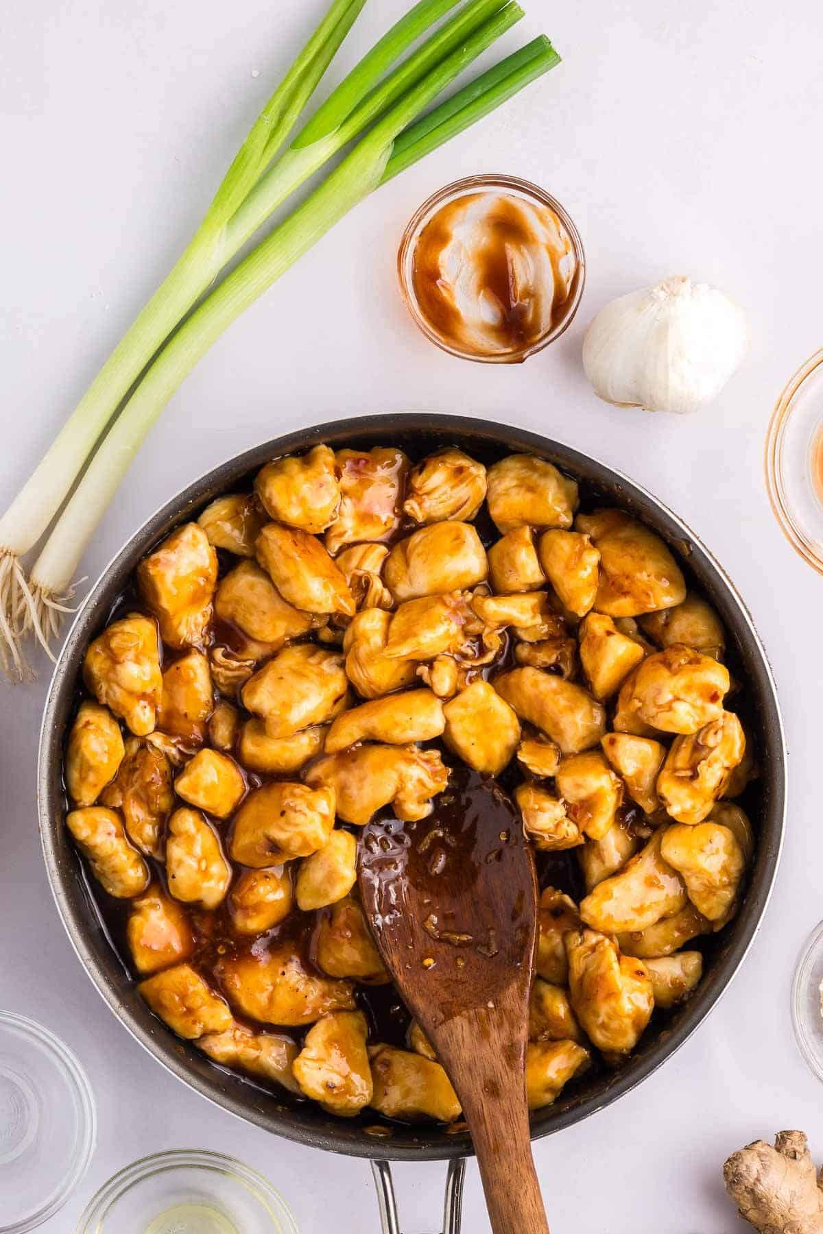 Chicken in a skillet with general tsaos sauce with a wooden spoon